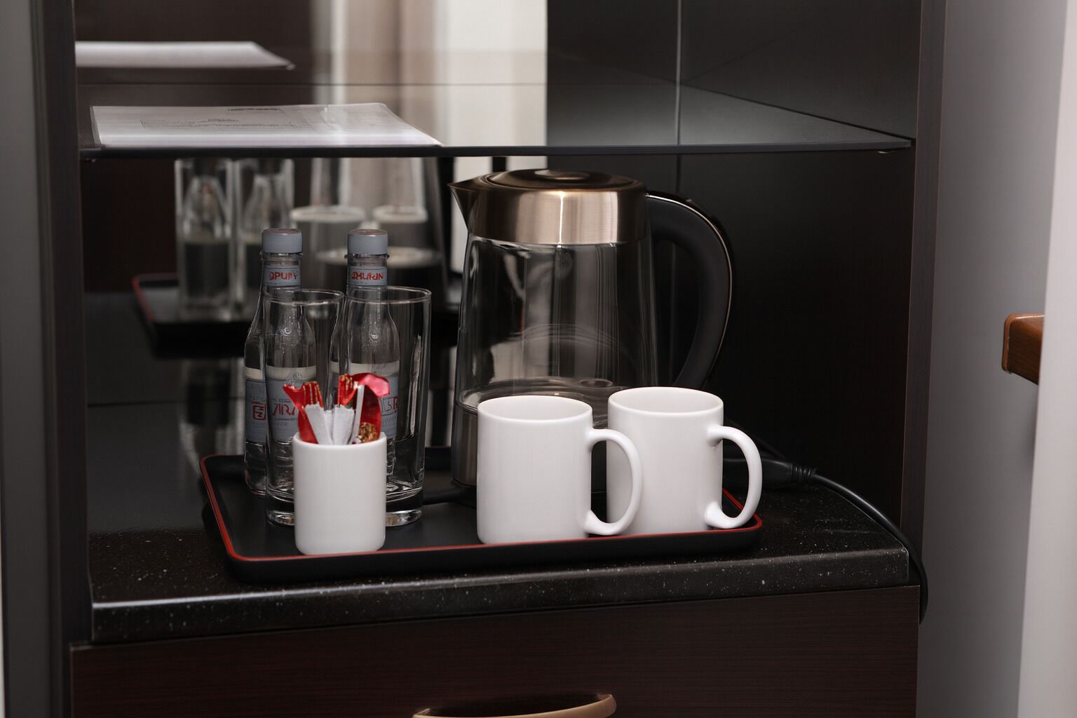 A coffee station with a coffee maker, two white mugs, and a glass container with utensils.