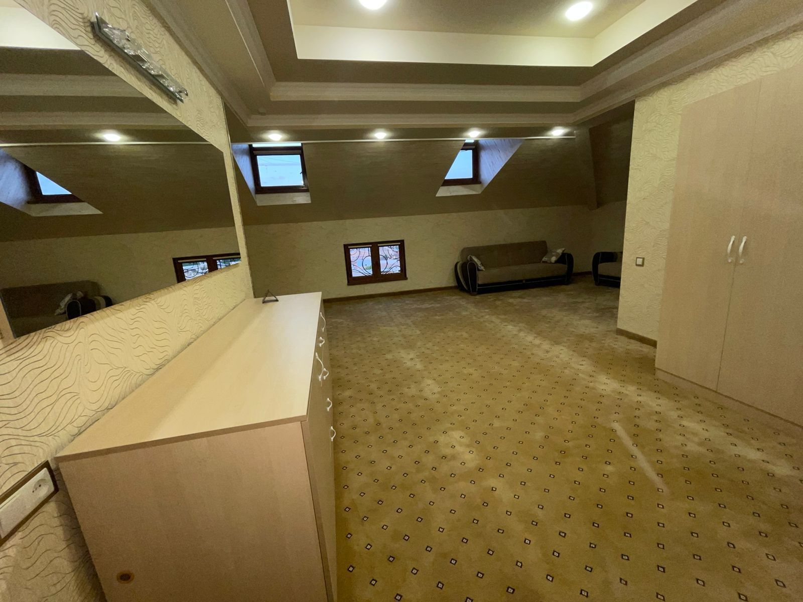 A spacious attic room with a high ceiling, skylights, a patterned carpet, a sofa, and a cabinet.
