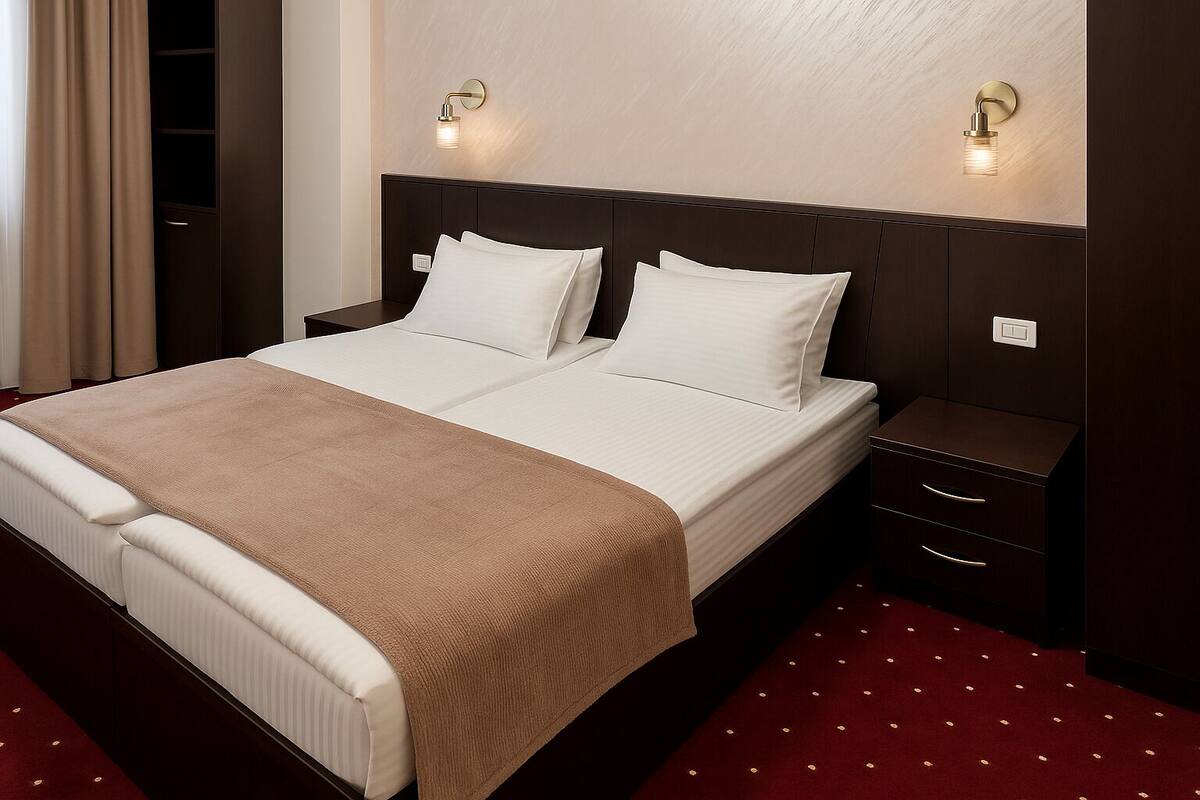 Ein Doppelbett mit brauner Tagesdecke, zwei Nachttische mit Lampen und ein roter Teppichboden.