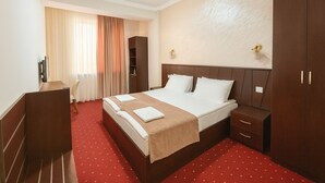 A hotel room with a large bed, a desk, a wardrobe, and a window with curtains. - Anga Yerevan Hotel (Yerevan)