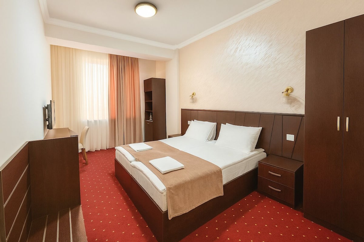 Ein Hotelzimmer mit einem großen Bett, einem Schreibtisch, einem Kleiderschrank und einem Fenster mit Vorhängen.