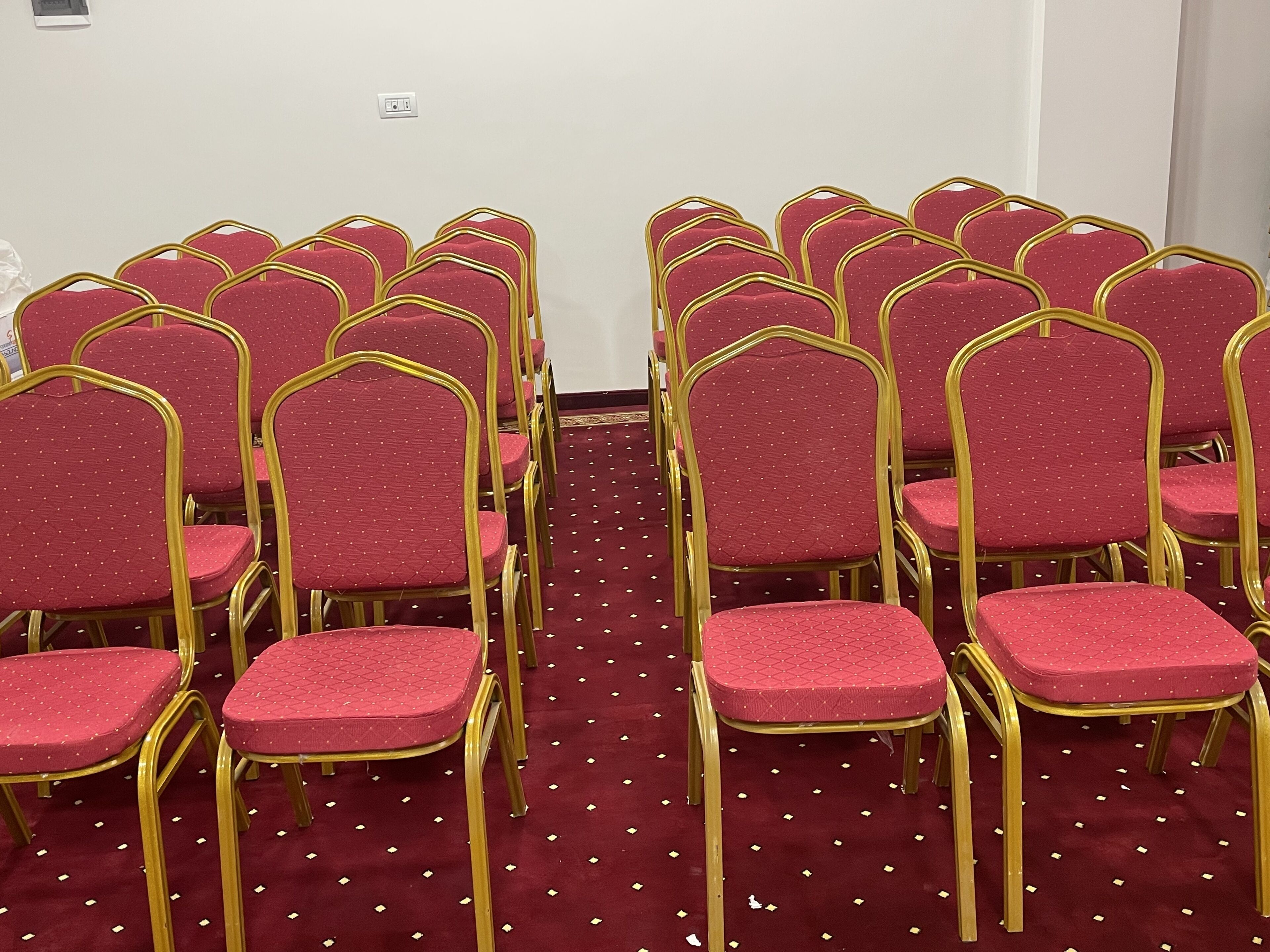 Rows of red chairs with gold frames arranged in a room with a red carpet.