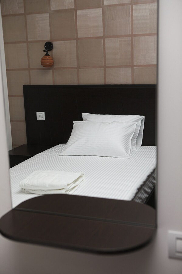 A neatly made bed with white linens, a dark headboard, and a small bedside table.