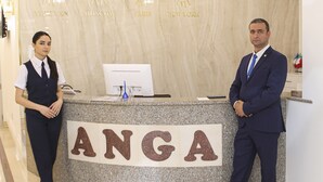 A reception desk with a marble wall and chandeliers. The desk has a sign that reads "ANGA". - Anga Yerevan Hotel (Yerevan)