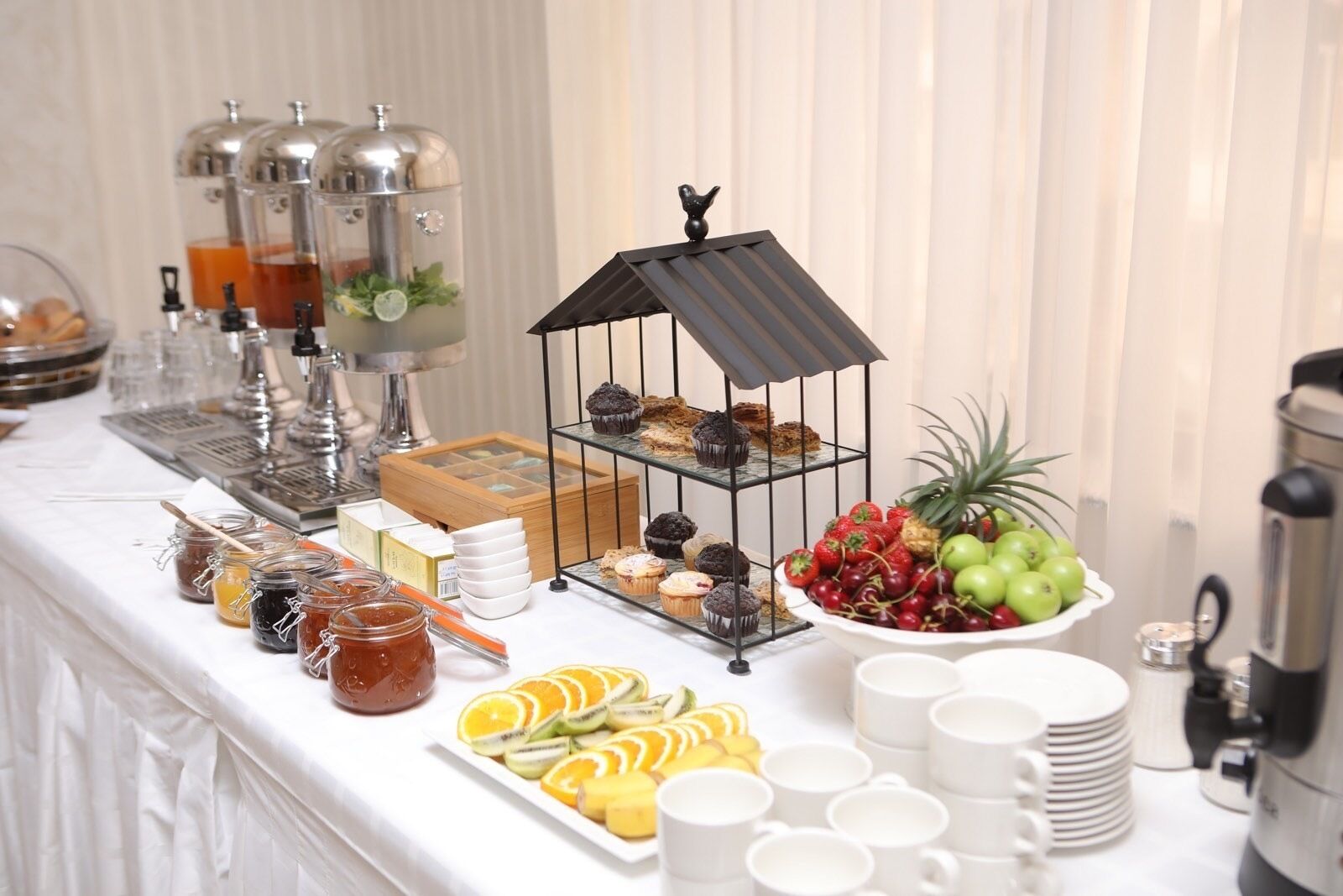 A buffet setup with various food items, including fruits, pastries, and condiments, arranged on a white table.