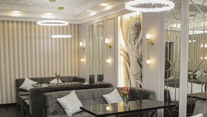A modern hotel lobby with grey upholstered sofas, a glass coffee table, and a large mirror reflecting the space. - Anga Yerevan Hotel (Yerevan)