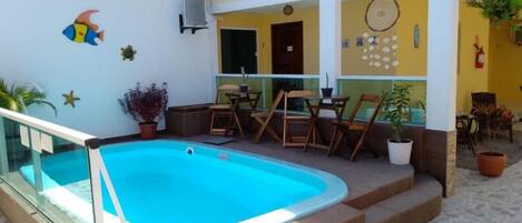 Piscina com barreira de vidro, deck de madeira e vasos de plantas.