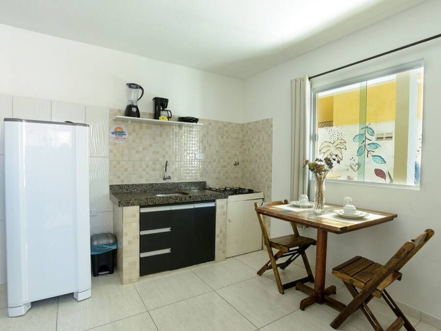 Uma cozinha compacta com geladeira, pia e uma pequena mesa de jantar com cadeiras.