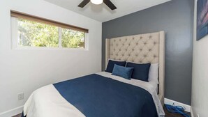 Een slaapkamer met een groot bed, een plafondventilator, een raam en een grijze muur.
