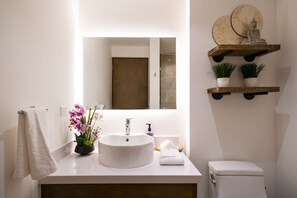 Un baño con un lavabo blanco, un espejo, un inodoro y un estante con objetos decorativos.