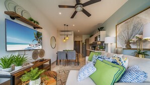 Una sala de estar moderna con un televisor de pantalla plana, un ventilador de techo y un comedor con sillas y una mesa.