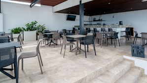 Un área de comedor al aire libre con varias mesas y sillas, una barra y plantas en macetas.