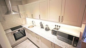 Uma cozinha moderna com armários brancos, um exaustor de aço inoxidável, forno, pia, chaleira e torradeira.