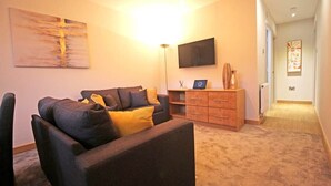 Uma sala de estar com sofá, televisão de tela plana, armário de madeira e um quadro na parede.