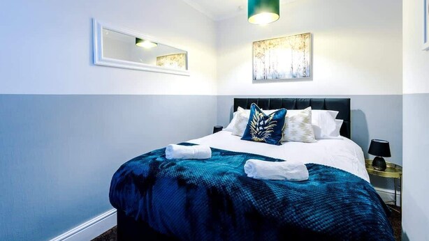 A neatly made bed with a blue and white duvet, a black headboard, and a wall-mounted mirror.