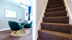 A staircase with dark patterned carpet, a dining area with teal chairs and a round table, and a window with a curtain.