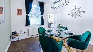 A dining area with a round table, green chairs, and a compass wall decoration.