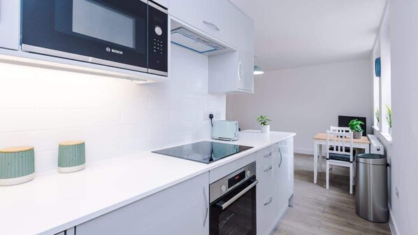 A modern kitchen with white cabinets, a Bosch microwave, a built-in oven, and a dining area with a table and chairs.