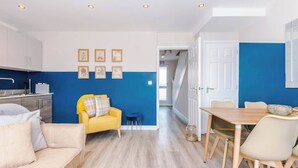 A modern kitchen with white cabinets, a yellow sofa, and a dining area with a wooden table and chairs. - Hidden Gem within Central Chester - Great Location (Chester)