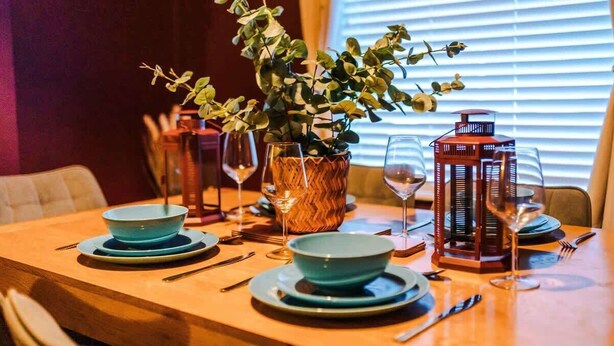 Mesa de jantar posta com tigelas azuis, copos de vinho e um lanterna vermelha.