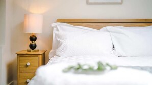 A neatly made bed with white linens and pillows, a bedside lamp on a wooden nightstand, and a framed picture on the wall. - 2BR Designer apartment for City Breaks in Chester. (Chester)
