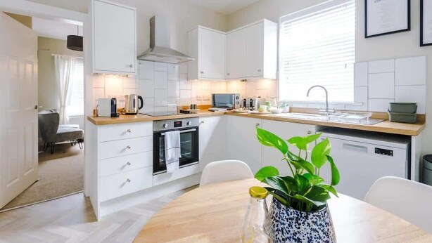 A modern kitchen with white cabinets, a wooden countertop, a built-in oven, and a sink. There is a dining table with chairs and a potted plant. - 2BR Designer apartment for City Breaks in Chester. (Chester)