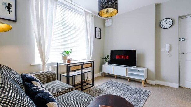 Ein Wohnzimmer mit einer Couch, einem Fernseher, einem Couchtisch und einem Fenster mit Vorhängen.