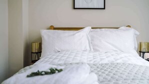 Ein ordentlich bezogenes Bett mit weißen Leinen und einer gesteppten Decke, das von zwei kleinen, runden Korbnächtichen mit Lampen eingerahmt wird.
