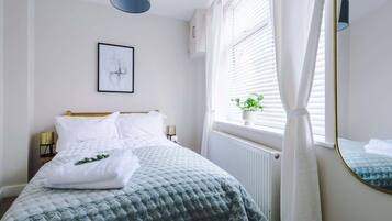 Cozy retreat with a neatly made bed, framed artwork, and a potted plant.