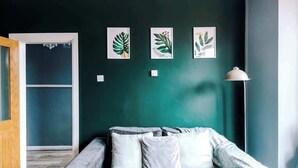 Une pièce avec un mur vert foncé, un canapé gris agrémenté de coussins blancs et trois reproductions botaniques encadrées.
