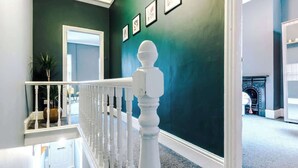 Un escalier avec des balustrades blanches menant à une pièce aux murs vert foncé, ornée de tableaux encadrés.