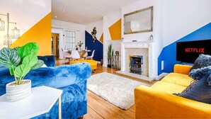 A modern living room with a blue and yellow color scheme, a fireplace, a television, and a dining area in the background. - Spacious 4 Bedroom Chester Home with parking. (Chester)