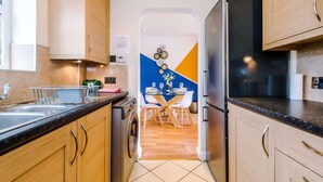 Une cuisine compacte avec des meubles en bois, un lave-vaisselle encastré et un coin repas comprenant une table et des chaises en verre.