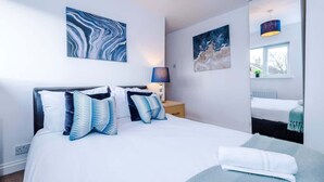 A modern bedroom with a large bed, a bedside table with a lamp, and artwork on the walls. - Spacious 4 Bedroom Chester Home with parking. (Chester)
