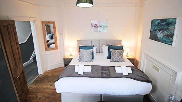 A bedroom with a large bed, two bedside tables, a mirror, and artwork on the walls.
