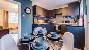 A modern kitchen with dark cabinetry, a microwave, and a coffee maker. There is a dining table set with blue plates and glasses.