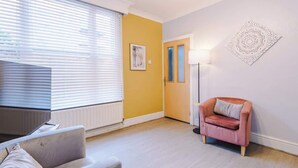 A modern living room with a sofa, a pink armchair, a floor lamp, and a painting on the wall.