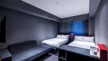 A modern hotel room with a sofa, two single beds, a desk with a red accent, and a TV mounted on the wall.