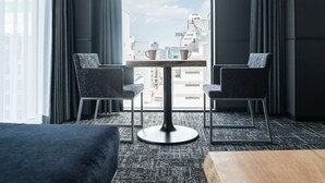 A hotel room with a view of the city, two chairs, a small table, and a bed. - Wyndham Garden Sapporo Odori (Sapporo)