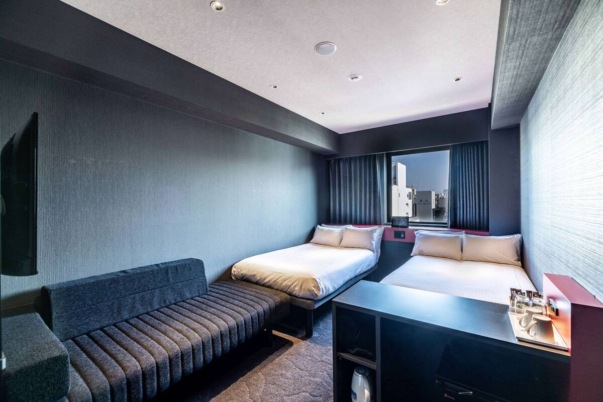 Ein modernes Hotelzimmer mit zwei Betten, einer Couch, einem Schreibtisch und einem Spiegel.