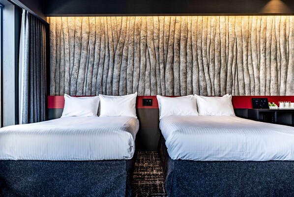 Une chambre d’hôtel avec deux lits, un mur à texture, un mur d’accent rouge et une petite table de chevet dotée d’un panneau de commande.