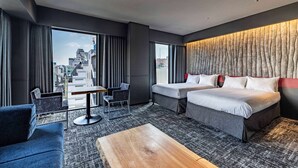 A modern hotel room with a large bed, a smaller bed, a sofa, a coffee table, and a view of the city through large windows. - Wyndham Garden Sapporo Odori (Sapporo)