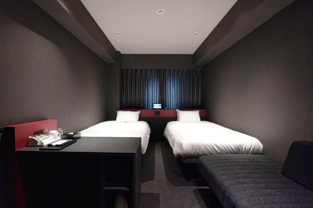 A hotel room with two beds, a desk, and a small couch.