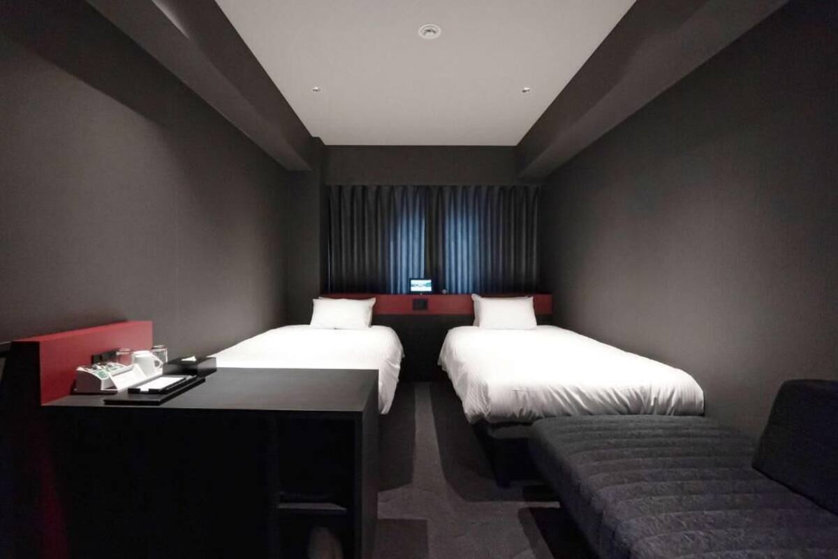 Ein Hotelzimmer mit zwei Betten, einem Schreibtisch und einer kleinen Couch.