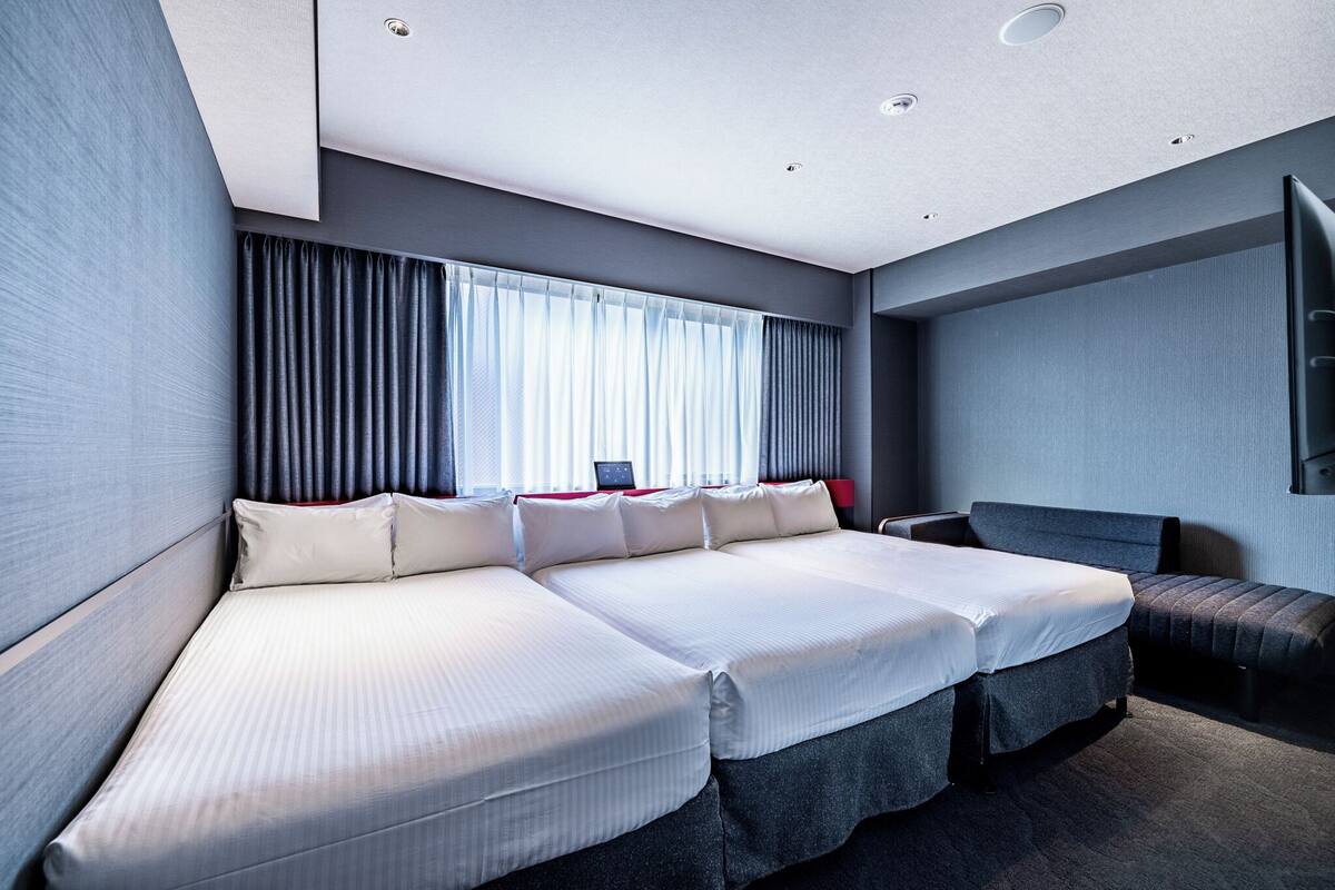 Ein modernes Hotelzimmer mit einem großen Bett, einem Nachttisch und einem großen Fenster mit Vorhängen.