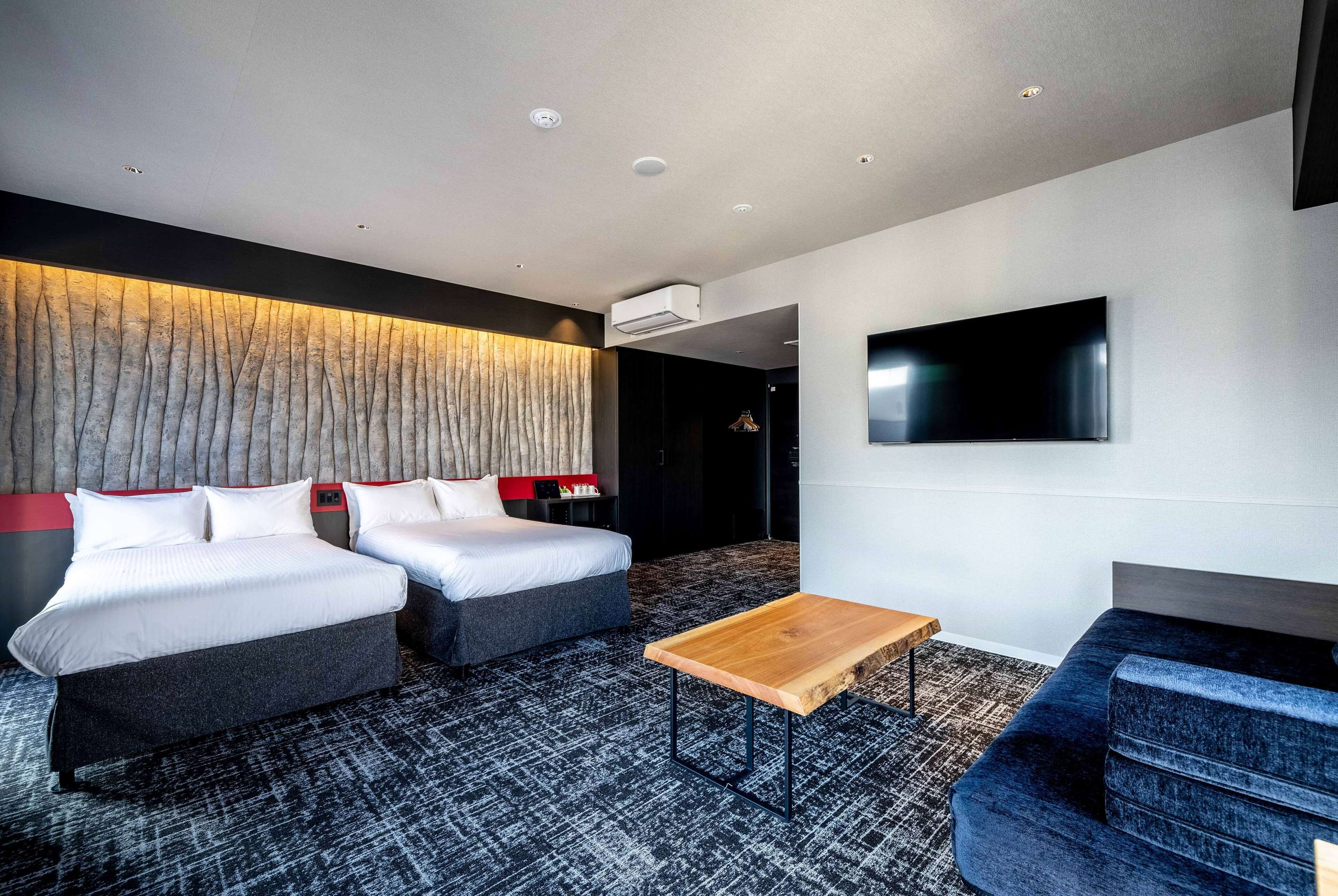 Una habitación de hotel moderna con dos camas, un televisor de pantalla plana, una mesa de centro de madera y una alfombra estampada.