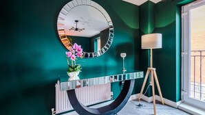 Une salle de bain aux murs de couleur turquoise, avec un miroir rond, un radiateur blanc, un meuble-lavabo noir, un lampadaire blanc et une fenêtre donnant sur un balcon.