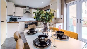 Een moderne keuken met witte kasten, een eettafel gedekt met zwart en goud servies, en een vaas met groene takken.