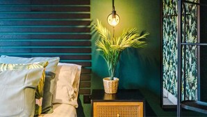 Un lit bien fait, agrémenté d’oreillers, une petite table de chevet avec une plante et une lampe, et un mur orné de lambris en bois verticaux.
