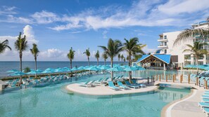 A resort pool area with multiple sun loungers and umbrellas, surrounded by palm trees and overlooking the ocean. - Margaritaville Island Reserve Riviera Maya - An Adults Only All Inclusive (Puerto Morelos)